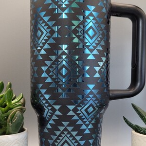 May include: A blue and black travel mug with a geometric pattern. The mug has a black handle and a black lid.