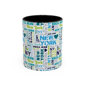Könnte beinhalten: Eine weiße Keramiktasse mit schwarzem Rand und Henkel. Die Tasse ist mit einem Muster aus den Wörtern "New York" in verschiedenen Blautönen, Grün- und Schwarztönen bedeckt. Die Wörter werden in einem zufälligen Muster wiederholt, wodurch ein geschäftiges und farbenfrohes Design entsteht.