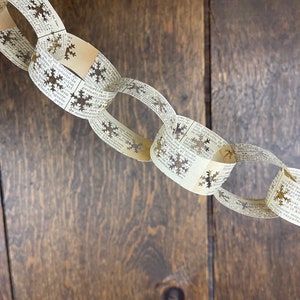 May include: A paper chain garland made from old book pages with snowflake cutouts. The garland is hanging against a woodgrain background.