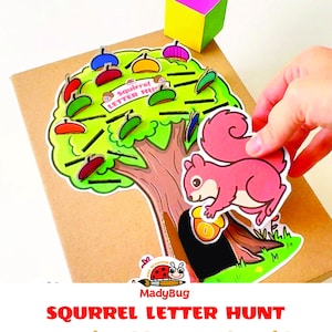 Peut inclure: Un jeu imprimable représentant un arbre vert avec des glands colorés et des lignes noires pour les lettres. Une découpe d'écureuil rose tient un gland près du tronc. Un petit cube jaune et violet est posé à côté. Le texte indique Squirrel Letter Hunt.