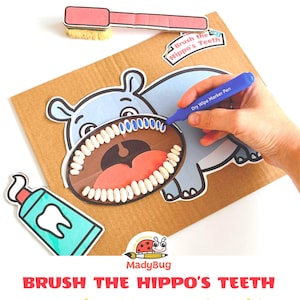Peut inclure: Un jeu imprimable intitulé Brush the Hippo's Teeth comprenant un hippopotame en carton avec des dents en haricots blancs, une brosse à dents rose, un tube de dentifrice bleu sarcelle et un feutre effaçable bleu. Texte Brush the Hippo's Teeth.
