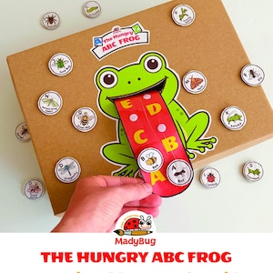 K&ouml;nnte beinhalten: Ein brauner Pappkarton mit einer gr&uuml;nen Froschillustration, deren lange rote Zunge die Buchstaben A bis E zeigt. Das Spiel enth&auml;lt runde Spielsteine mit Insektenabbildungen und Beschriftungen. Der Text lautet The Hungry ABC FROG.