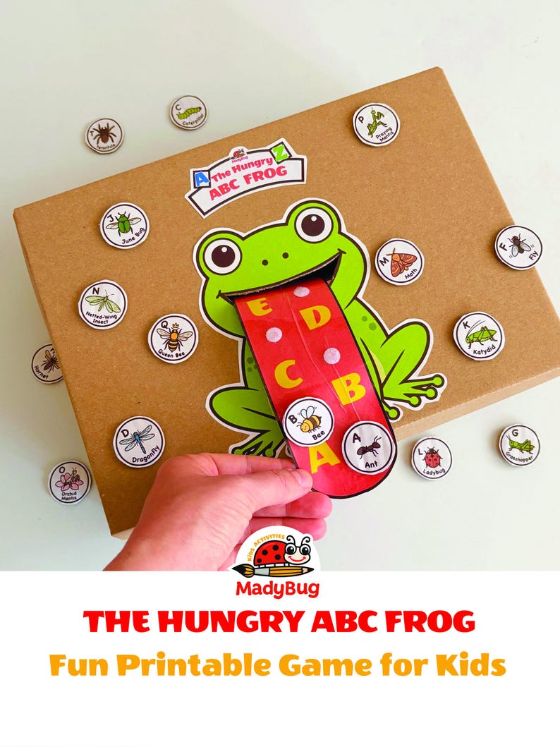 K&ouml;nnte beinhalten: Ein brauner Pappkarton mit einer gr&uuml;nen Froschillustration, deren lange rote Zunge die Buchstaben A bis E zeigt. Das Spiel enth&auml;lt runde Spielsteine mit Insektenabbildungen und Beschriftungen. Der Text lautet The Hungry ABC FROG.