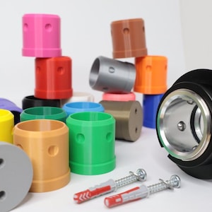 Puede incluir: Surtido de tapas de plástico de colores con dos agujeros, una base de metal negro con un anillo plateado y dos tornillos rojos y blancos.