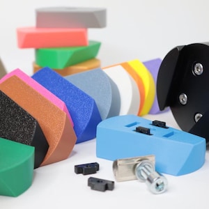 Könnte beinhalten: Sortiment an bunten Schaumstoffpolstern in verschiedenen Formen und Größen, darunter ein schwarzes Schaumstoffpolster mit einem Loch in der Mitte. Ein schwarzes Werkzeug mit einem dreizackigen Kopf ist ebenfalls abgebildet.