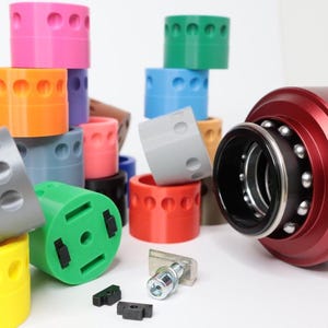 May include: An assortment of colourful plastic rings stacked in a tower, with a red metal bearing assembly with the word "SIMAGIC" on the side.