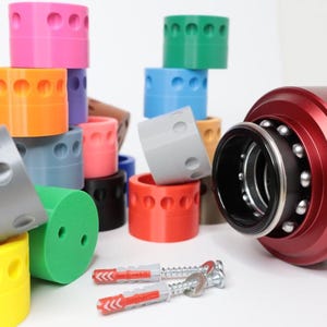 May include: An assortment of colourful plastic rings with a red metal object with the word "SIMAGIC" on it. The metal object has a black ring with ball bearings around it. There are also two red and white screws and a silver screw.