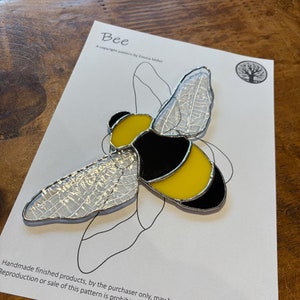 May include: A stained glass bee with black, yellow, and clear glass. The bee is on a white background with the text "Bee" and "A copyright pattern by Emma Miller".