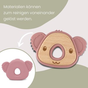 May include: A pink and wood-toned koala-shaped baby teether. The teether has a circular center and a koala face design with small ears and a smiling mouth. The text in the image says, "Materials can be removed for cleaning."