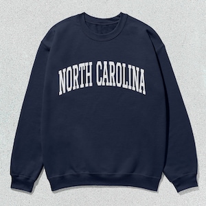 Pu&ograve; includere: Una felpa blu navy con la scritta "NORTH CAROLINA" in lettere bianche sul davanti.