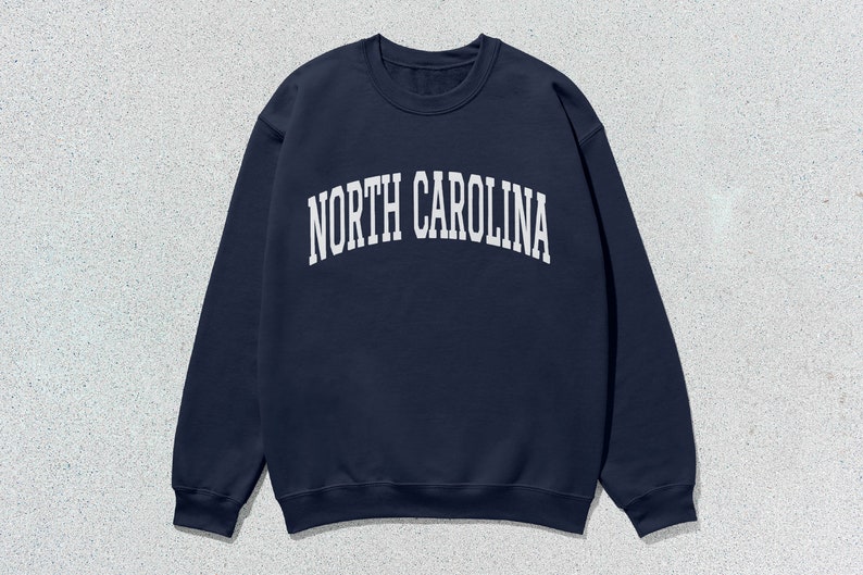 Pu&ograve; includere: Una felpa blu navy con la scritta "NORTH CAROLINA" in lettere bianche sul davanti.