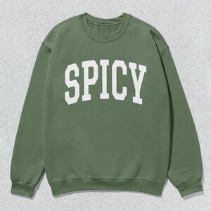 Może przedstawiać: Zielony sweter z nadrukiem "SPICY" w kolorze białym z przodu.