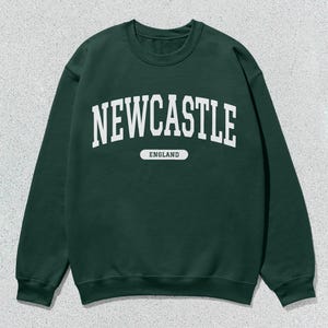 K&ouml;nnte beinhalten: Ein dunkelgr&uuml;ner Pullover mit wei&szlig;em Text, der "NEWCASTLE ENGLAND" lautet.