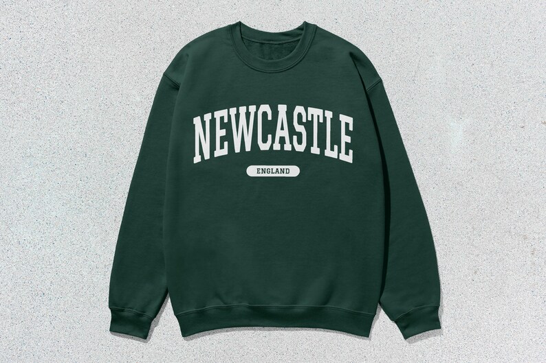 K&ouml;nnte beinhalten: Ein dunkelgr&uuml;ner Pullover mit wei&szlig;em Text, der "NEWCASTLE ENGLAND" lautet.
