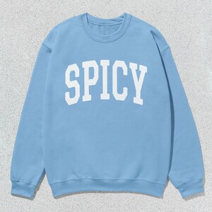 Może przedstawiać: Jas sportowy w jasnoniebieskim kolorze z nadrukiem "SPICY" w kolorze białym z przodu.