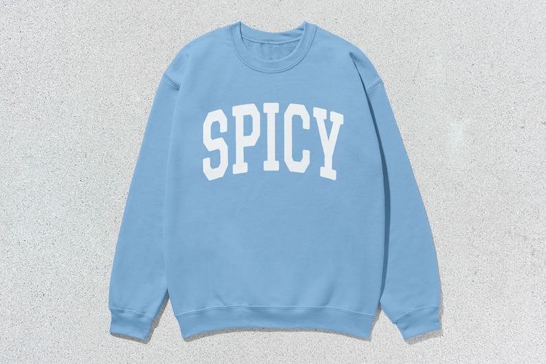 Może przedstawiać: Jas sportowy w jasnoniebieskim kolorze z nadrukiem "SPICY" w kolorze białym z przodu.