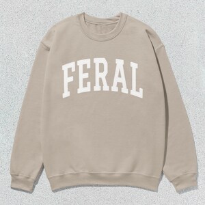 May include: A beige sweatshirt with the word "FERAL" printed in white on the front.