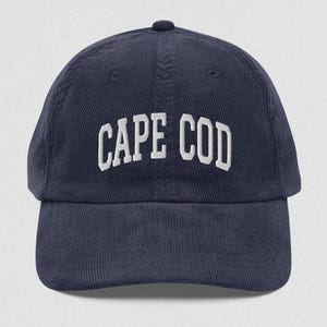 May include: A navy blue corduroy baseball cap with white embroidered text that reads "CAPE COD".