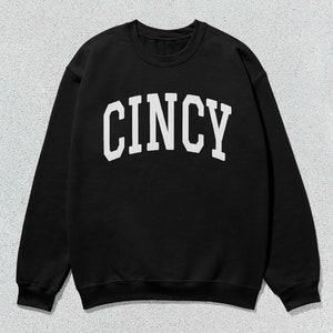 Puede incluir: Sudadera negra con texto blanco que dice "CINCY" en una fuente universitaria.