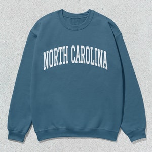 Pu&ograve; includere: Una felpa blu con la scritta "NORTH CAROLINA" stampata in bianco sul davanti.