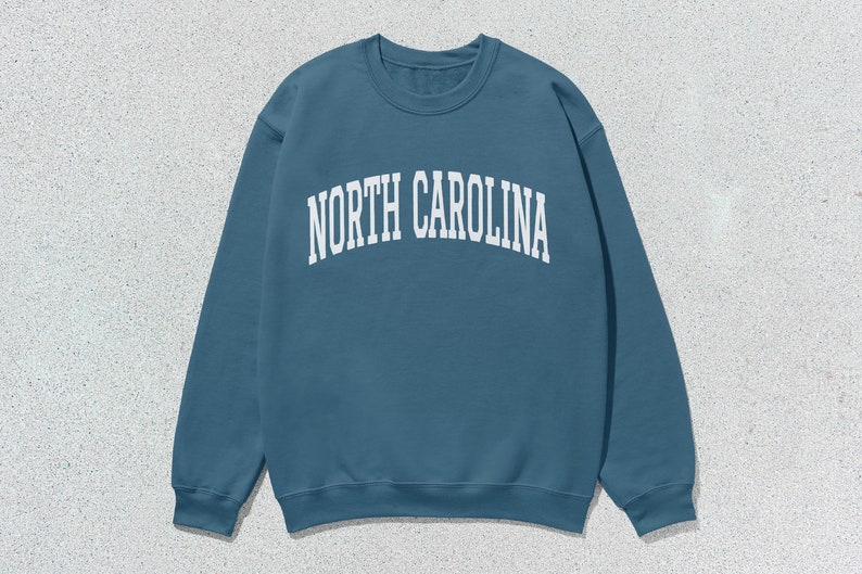 Pu&ograve; includere: Una felpa blu con la scritta "NORTH CAROLINA" stampata in bianco sul davanti.