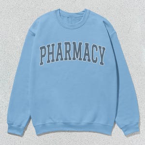 May include: A light blue sweatshirt with the word "PHARMACY" printed in dark gray across the front.