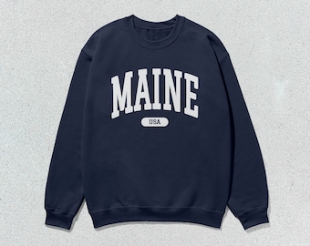 May include: A navy blue sweatshirt with a white print that says "MAINE USA" in a collegiate style font.