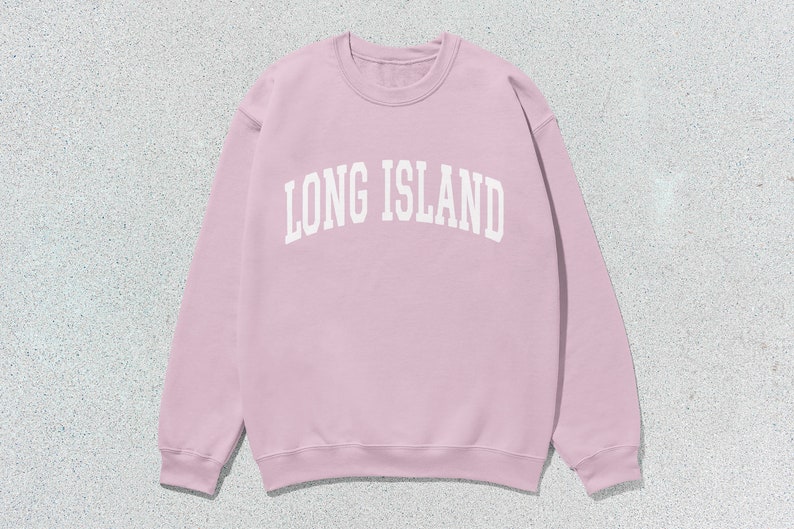Pu&ograve; includere: Una felpa rosa chiaro con la scritta bianca "LONG ISLAND" in caratteri arcuati. La felpa girocollo &egrave; di colore uniforme e ha maniche lunghe. L'immagine &egrave; ripresa dall'alto.