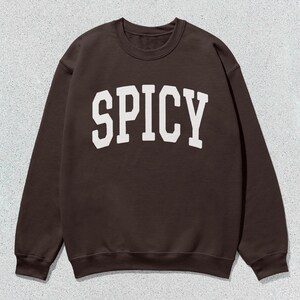 Może przedstawiać: Brązowa bluza z nadrukiem "SPICY" w kolorze białym na przodzie.