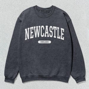 K&ouml;nnte beinhalten: Ein dunkelgrauer Pullover mit wei&szlig;em Text, der "NEWCASTLE ENGLAND" lautet.