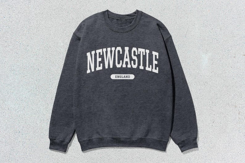 K&ouml;nnte beinhalten: Ein dunkelgrauer Pullover mit wei&szlig;em Text, der "NEWCASTLE ENGLAND" lautet.