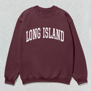 Pu&ograve; includere: Una felpa bordeaux girocollo con la scritta "LONG ISLAND" in bianco, a lettere arcuate. La felpa &egrave; realizzata in un materiale morbido e ha uno stile classico e casual. Lo sfondo &egrave; una superficie screziata grigio chiaro.