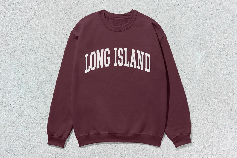 Pu&ograve; includere: Una felpa bordeaux girocollo con la scritta "LONG ISLAND" in bianco, a lettere arcuate. La felpa &egrave; realizzata in un materiale morbido e ha uno stile classico e casual. Lo sfondo &egrave; una superficie screziata grigio chiaro.