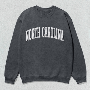Pu&ograve; includere: Una felpa grigia scura con la scritta "NORTH CAROLINA" stampata in bianco sul davanti.