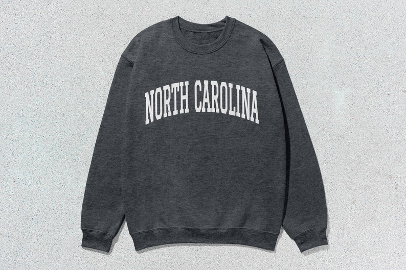 Pu&ograve; includere: Una felpa grigia scura con la scritta "NORTH CAROLINA" stampata in bianco sul davanti.