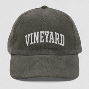 May include: A dark green corduroy baseball cap with white embroidered text that reads "VINEYARD".