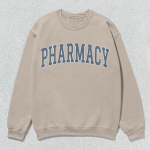 May include: A tan sweatshirt with the word "PHARMACY" printed in blue on the front.