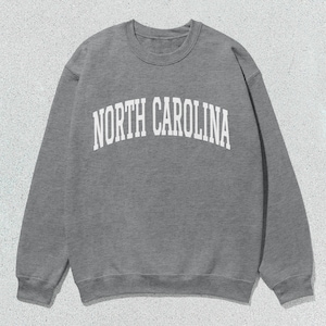 Pu&ograve; includere: Una felpa grigia con la scritta "NORTH CAROLINA" stampata in bianco sul davanti.