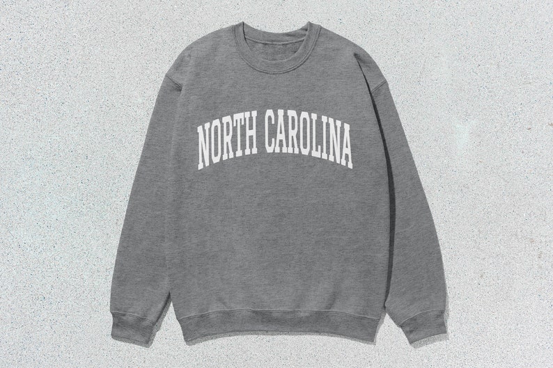 Pu&ograve; includere: Una felpa grigia con la scritta "NORTH CAROLINA" stampata in bianco sul davanti.