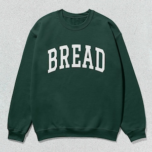 Puede incluir: Una sudadera verde oscuro con la palabra "BREAD" impresa en blanco en la parte delantera.