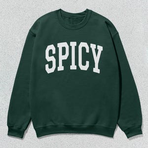 Może przedstawiać: Zielony sweter z nadrukiem "SPICY" w kolorze białym na przodzie.
