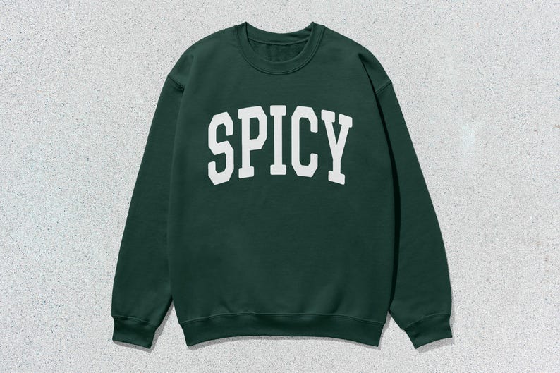 Może przedstawiać: Zielony sweter z nadrukiem "SPICY" w kolorze białym na przodzie.