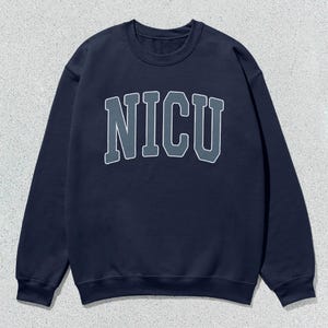 Puede incluir: Sudadera azul marino con cuello redondo y la palabra "NICU" en una fuente de estilo universitario en el pecho. Las letras son grises con un contorno blanco. La sudadera tiene mangas largas y un cuello acanalado.
