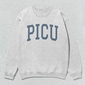 Puede incluir: Una sudadera gris con la palabra "PICU" impresa en azul en la parte delantera.