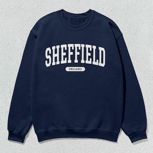 以下が含まれることがあります： アーチ型のフォントで「SHEFFIELD ENGLAND」と書かれた白いテキストが入ったネイビーブルーのスウェットシャツです。