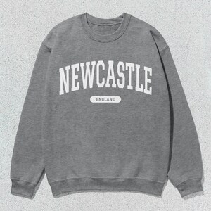 K&ouml;nnte beinhalten: Grauer Sweatshirt mit wei&szlig;em Text, der "NEWCASTLE ENGLAND" lautet.