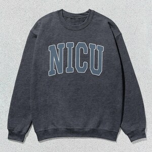 Puede incluir: Sudadera gris oscuro con la palabra "NICU" en letras grandes en el pecho. Las letras son de un gris m&aacute;s claro con un contorno blanco. La sudadera tiene cuello redondo y mangas largas.