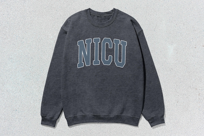 Puede incluir: Sudadera gris oscuro con la palabra "NICU" en letras grandes en el pecho. Las letras son de un gris m&aacute;s claro con un contorno blanco. La sudadera tiene cuello redondo y mangas largas.