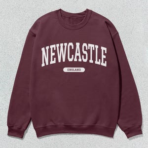 K&ouml;nnte beinhalten: Ein weinroter Pullover mit wei&szlig;em Text, der "NEWCASTLE ENGLAND" lautet.