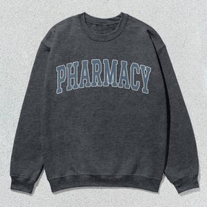 May include: A dark gray sweatshirt with the word "PHARMACY" printed in a light blue and gray arch across the front.